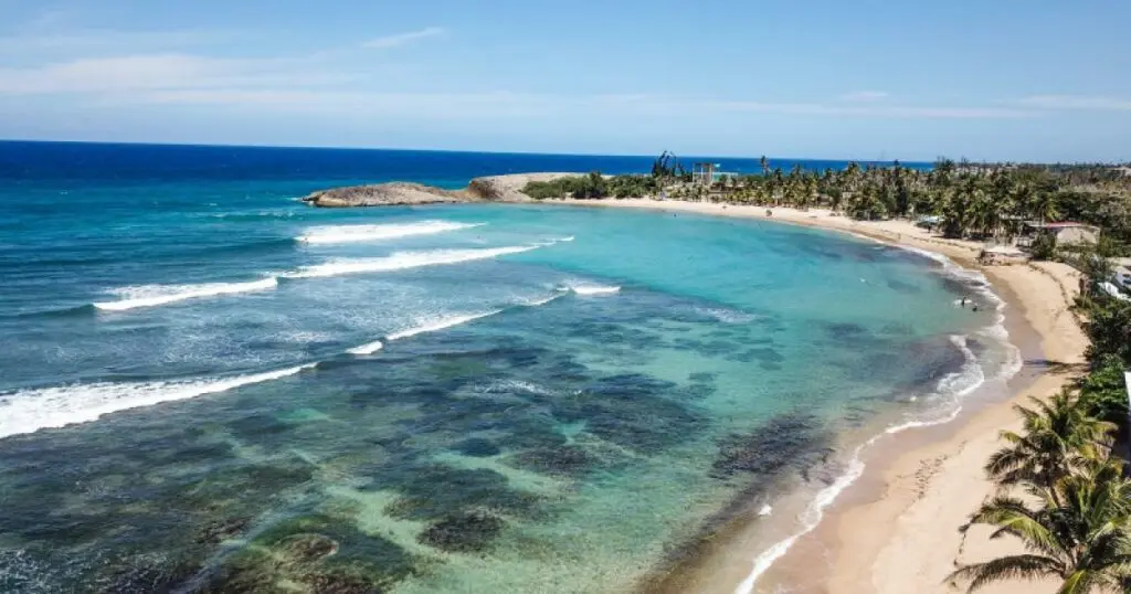 The beach itself is a beautiful stretch of golden sand, contrasting with the clear blue waters. Surfers will find challenging waves, while families can enjoy calmer areas for swimming and sunbathing.  